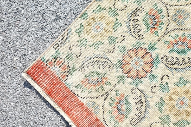 May include: Close-up of a section of a vintage rug with a cream-colored background. The rug features floral patterns in shades of orange, green, and blue, with a red border. The design is intricate and detailed, showcasing a classic aesthetic.