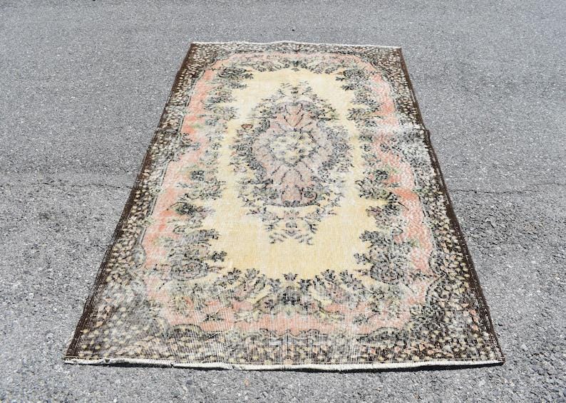 May include: Rectangular rug with a central floral medallion in cream, surrounded by a border of pink and black floral patterns. The rug has a distressed, vintage appearance, with a dark brown border.