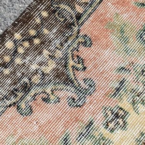 May include: Close-up of a section of a vintage rug with a detailed, woven pattern. The rug features a color palette of brown, peach, green, and cream. The design includes floral and geometric elements, creating a textured, antique aesthetic.