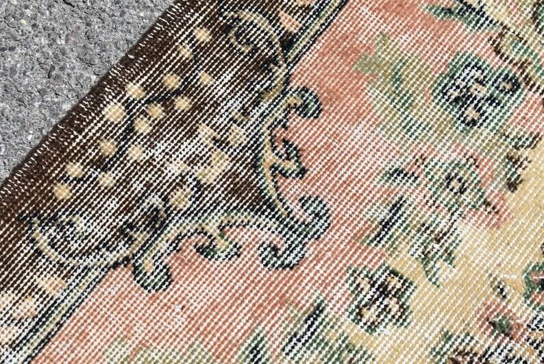 May include: Close-up of a section of a vintage rug with a detailed, woven pattern. The rug features a color palette of brown, peach, green, and cream. The design includes floral and geometric elements, creating a textured, antique aesthetic.