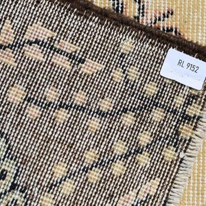 May include: Close-up of a section of a vintage rug with a detailed geometric pattern in beige, black, and brown. The rug's edge is visible, along with a tag that reads "RL 9152". The rug has a distressed, antique appearance.