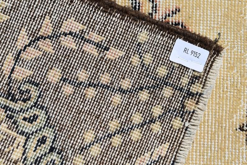 May include: Close-up of a section of a vintage rug with a detailed geometric pattern in beige, black, and brown. The rug's edge is visible, along with a tag that reads "RL 9152". The rug has a distressed, antique appearance.