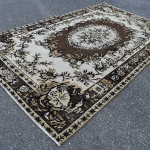 May include: A vintage rug with a brown and white floral pattern. The rug has a central medallion and a border with a geometric design.