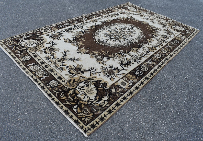 May include: A vintage rug with a brown and white floral pattern. The rug has a central medallion and a border with a geometric design.