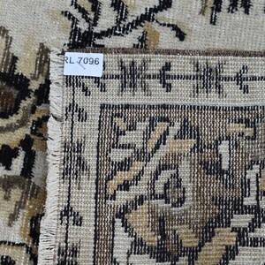 May include: Close-up of a beige rug with a brown and black floral pattern. The rug has a fringe border and a label that reads "RL 7096".