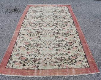 May include: A vintage floral patterned rug with a cream background and a red border. The rug has a faded look and is made of wool.
