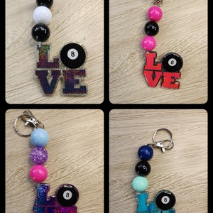 May include: Four different keychains with the word "LOVE" spelled out in colorful glitter letters. Each keychain has a black 8-ball charm and a variety of colorful beads.
