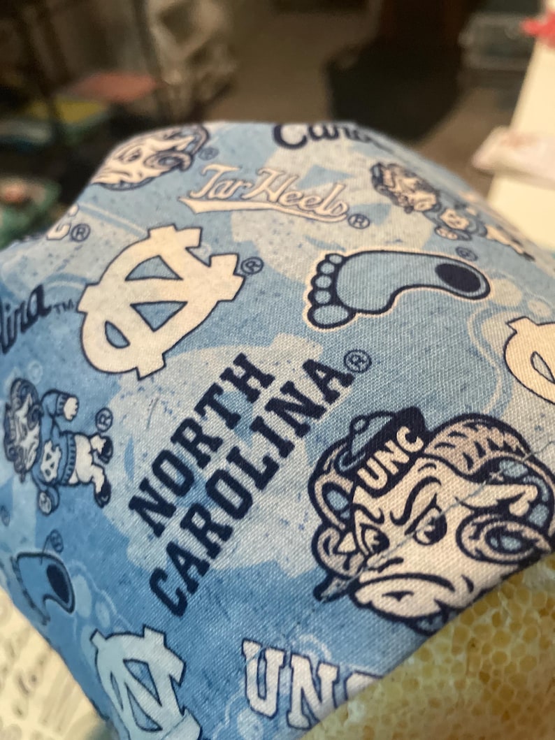 May include: Light blue fabric with a repeating pattern of white logos, text, and illustrations associated with the University of North Carolina. The words "North Carolina" and "UNC" are visible.