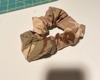 Puede incluir: Un coletero de tela con un estampado de camuflaje en tonos beige, marrón y arena. El coletero está colocado junto a una regla de corte de la marca Dritz que muestra medidas en centímetros.