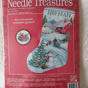 May include: A Needle Treasures counted cross stitch kit for an Evergreen Outing stocking, featuring a winter scene with a snowman, a red barn, and the name Norman. The package includes a free ornament, with a finished size of 10 inches by 16 inches.
