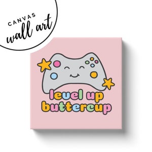 May include: A pink canvas wall art print featuring a smiling gray video game controller with colorful buttons and star accents. The text "level up buttercup" is below the controller. The words "canvas wall art" are in a circle in the upper left corner.