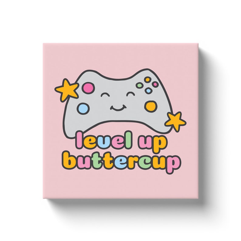 May include: A pink canvas print featuring a smiling gray video game controller with colorful buttons and two yellow stars. The text "level up buttercup" is written below the controller in various colors.
