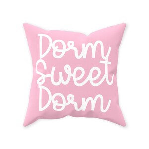 May include: A pink throw pillow with the text "Dorm Sweet Dorm" in white cursive lettering.