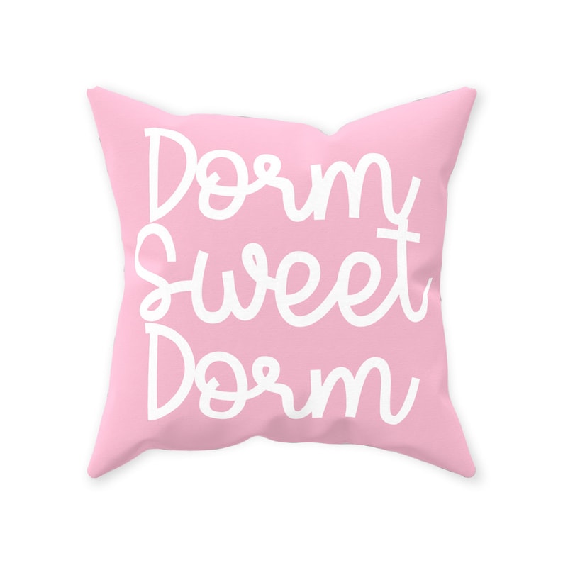 May include: A pink throw pillow with the text "Dorm Sweet Dorm" in white cursive lettering.