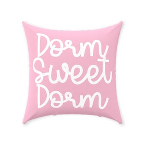 May include: A pink throw pillow with the text "Dorm Sweet Dorm" in white cursive lettering.