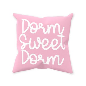 May include: A pink throw pillow with the text "Dorm Sweet Dorm" in white cursive lettering.