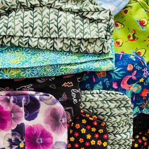 May include: A collection of fabric squares with various patterns, including green leaves, blue flowers, a mermaid, and a black and white design with the word "love".