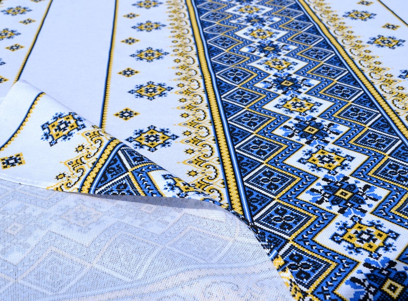 May include: White fabric with a blue and yellow geometric pattern. The fabric has a repeating design of squares and diamonds.