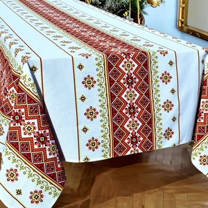 May include: White tablecloth with a red, yellow and green embroidered pattern. The tablecloth is laid on a wooden table.