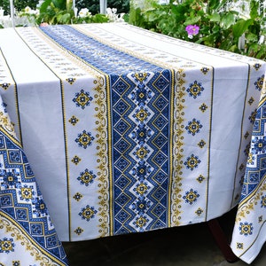 May include: White tablecloth with a blue and yellow geometric pattern. The tablecloth has a traditional embroidered design.