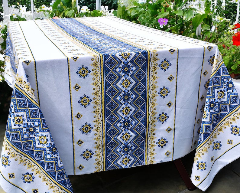May include: White tablecloth with a blue and yellow geometric pattern. The tablecloth has a traditional embroidered design.