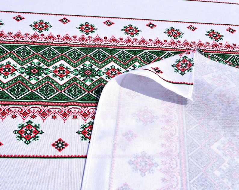 May include: White fabric with a green and red embroidered pattern. The fabric is folded over, revealing the white underside.