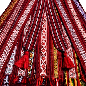 Op de afbeelding: Een verzameling van rood, wit en zwart geweven riemen met ingewikkelde geometrische patronen. De riemen hebben kwastjes aan de uiteinden en zijn waaiervormig gerangschikt.