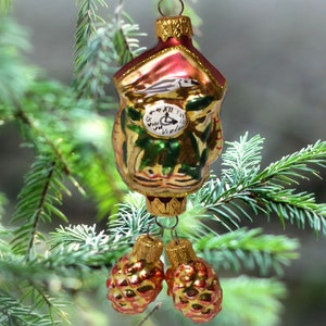 May include: A gold and red glass Christmas ornament shaped like a cuckoo clock with a bird on top and two gold pine cone ornaments hanging from the bottom.
