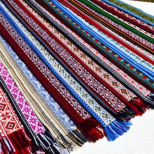 May include: A collection of colorful woven fabric strips with intricate patterns. The strips are arranged in a fan shape and have fringed edges.