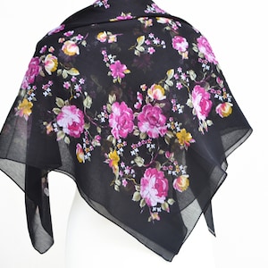 Op de afbeelding: Een zwarte, doorschijnende sjaal met een bloemenprint met roze en gele rozen.