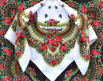 May include: A white square scarf with a vibrant floral design, featuring red roses, green leaves, and blue accents. The scarf has a detailed border and is displayed on a hanger, showcasing its intricate pattern.