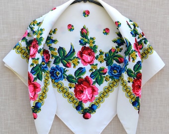 May include: White square scarf with a floral pattern. The design features large pink and red roses, blue flowers, green leaves, and yellow accents. A gold chain-like border frames the floral arrangement. The scarf is displayed on a black hanger.