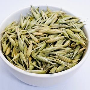 May include: A white bowl filled with dried oat groats, a type of whole grain.