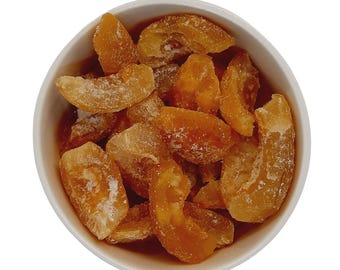 May include: A white bowl filled with candied fruit. The fruit pieces are a light amber color, with a sugared coating. The bowl is set against a white background, highlighting the food's texture and color.