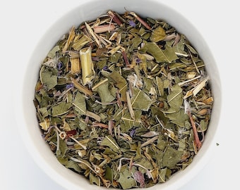 May include: A white bowl filled with a blend of dried herbs and flowers, including green leaves, brown stems, and purple flower petals.