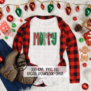 May include: A white t-shirt with the word "Merry" in red, green, and white patterned letters. The shirt is laid out on a red and black plaid shirt with Christmas decorations around it.