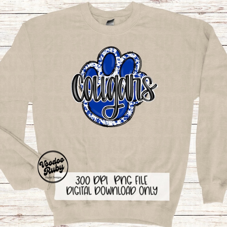 May include: A beige sweatshirt with a blue and white paw print design. The word "cougars" is written in black lettering on the paw print.