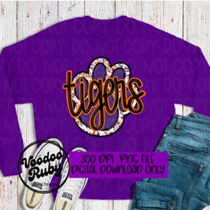 May include: Purple sweatshirt with a black and orange paw print with the word "tigers" in black lettering. The image is a digital download.