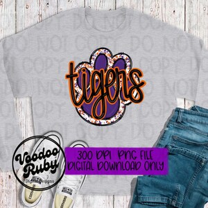 May include: A purple and orange paw print with the word "tigers" in black text. The paw print is on a gray sweatshirt.