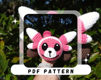May include: A handmade crochet plushie in pink, white, and brown, resembling a cartoon character. The plushie has large, white-tipped ears and a smiling face with black eyes. The text "PDF PATTERN" is displayed on the image.