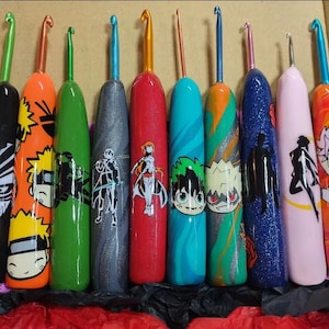 May include: A collection of ten crochet hooks with colorful handles. Each hook features a unique design, including anime characters and patterns. The hooks have metal tips and are arranged in a box, showcasing a variety of colors and styles.