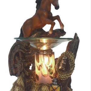 May include: A brown horse figurine stands atop a wooden base with a glass bowl for essential oils. The base features a wagon wheel, rope, and a lantern.