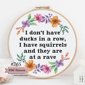 May include: A white embroidery hoop with a floral design and the text "I don't have ducks in a row, I have squirrels and they are at a rave". The hoop is surrounded by a wooden frame.