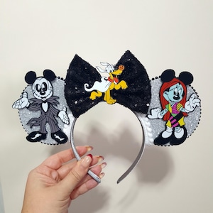 May include: Silver glitter Mickey Mouse ears with a black bow, featuring a black and white Jack Skellington character on one ear and a colorful Sally character on the other ear. A yellow Pluto character is on the bow.