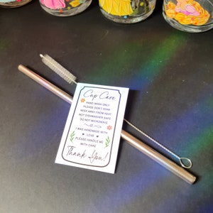 May include: A white card with the text "Cup Care" and instructions for hand washing, soaking, heat, dishwasher, and microwave use. The card also includes the text "I was handmade with love. Please handle me with care. Thank You!"  A stainless steel straw and a cleaning brush are also pictured.