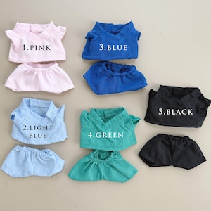 Puede incluir: Conjunto de ropa para muñecas en varios colores: rosa, azul claro, azul, verde y negro. Cada conjunto consta de una parte superior con cuello en V y una falda o pantalón corto a juego. Los conjuntos están etiquetados con números y nombres de colores.