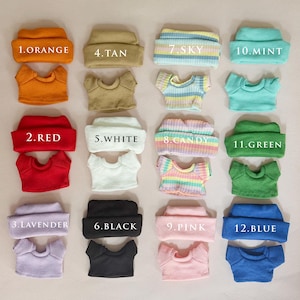 Puede incluir: Una colección de gorros y camisetas de manga corta a juego, de punto acanalado para muñecas, en varios colores. Los colores incluyen naranja, rojo, lavanda, beige, blanco, negro, azul cielo, caramelo, rosa, menta, verde y azul. Cada artículo está etiquetado con un número y un nombre de color.