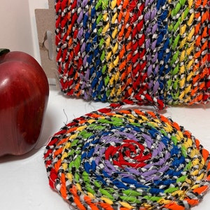 May include: A colorful braided rug with a spiral pattern in black, white, red, yellow, green, and blue. The rug is made from fabric scraps and has a rustic, handmade look.