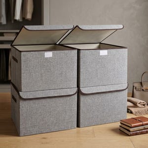 May include: Four rectangular storage bins made of grey fabric with dark brown trim. Each bin features a hinged lid that opens upward and a small white rectangular label holder on the front. The bins are arranged in two stacks of two units each.