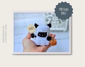 May include: A crocheted Halloween cat in a ghost costume holding a wooden sign that says "Boo!" and a small orange pumpkin. The cat has black ears and eyes. The image is labeled "meowloween buddy."